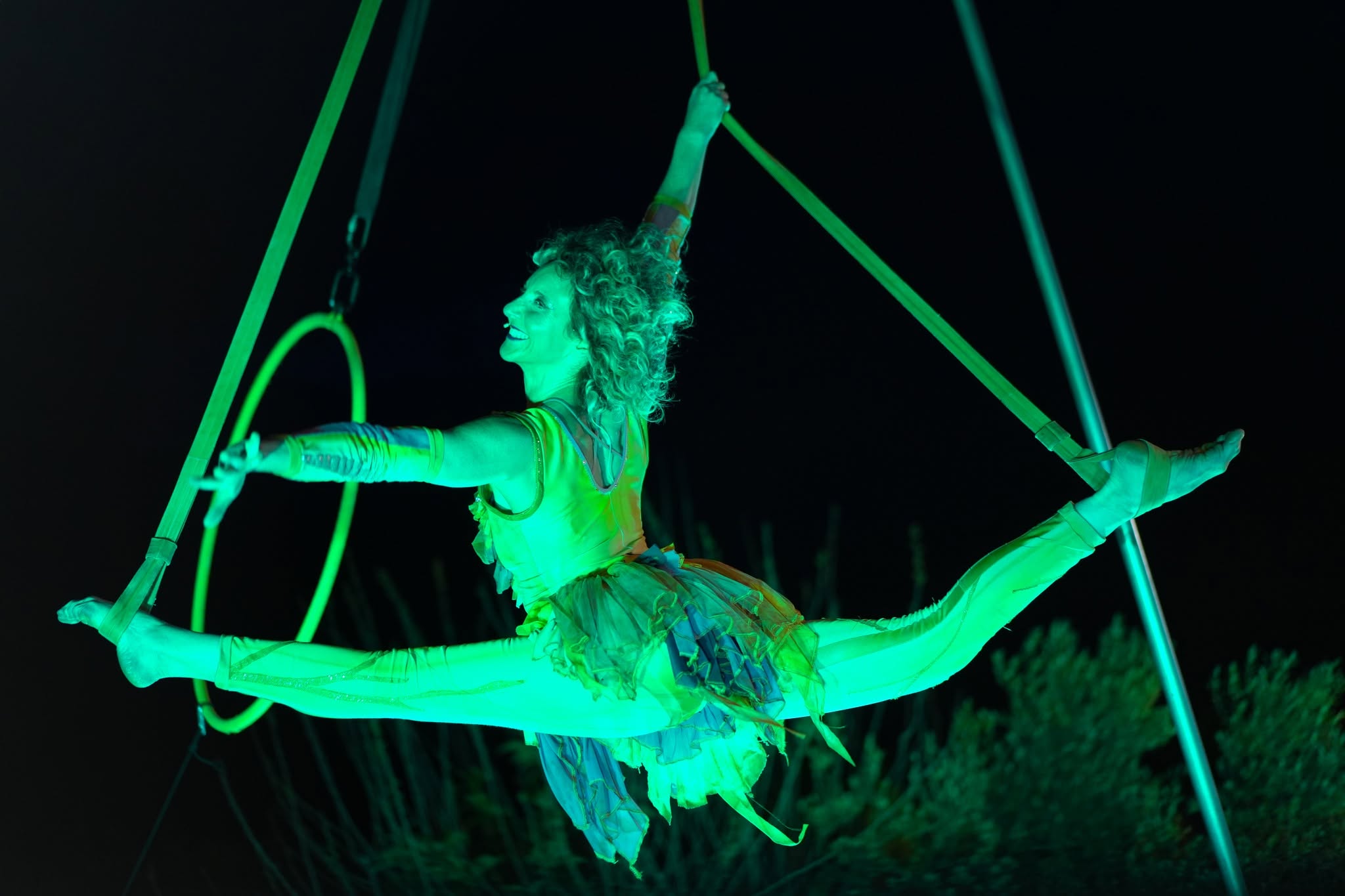 An acrobat performs in the air on a green-lit apparatus.