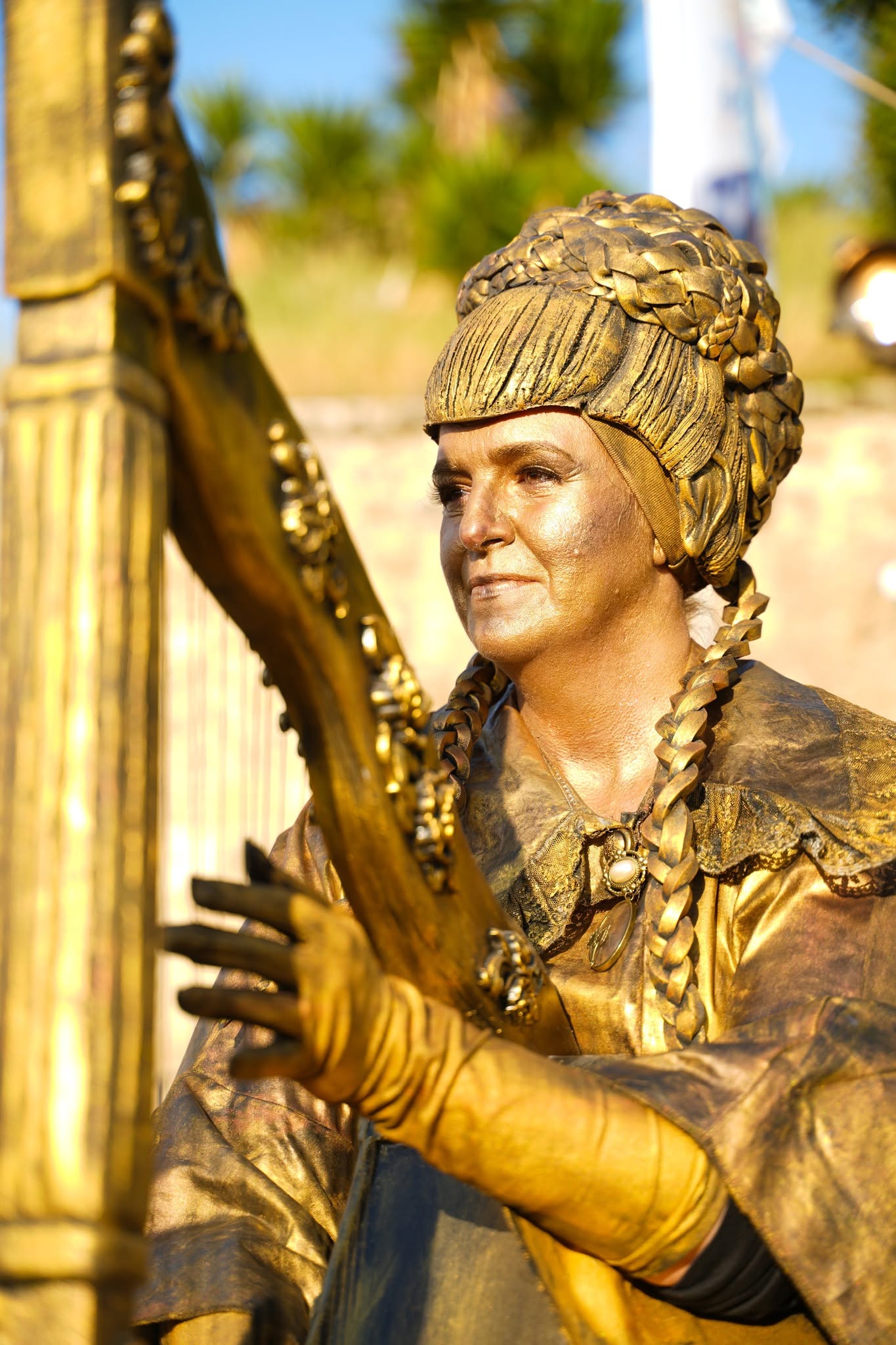 A musician in a gold costume performs in the street by day.