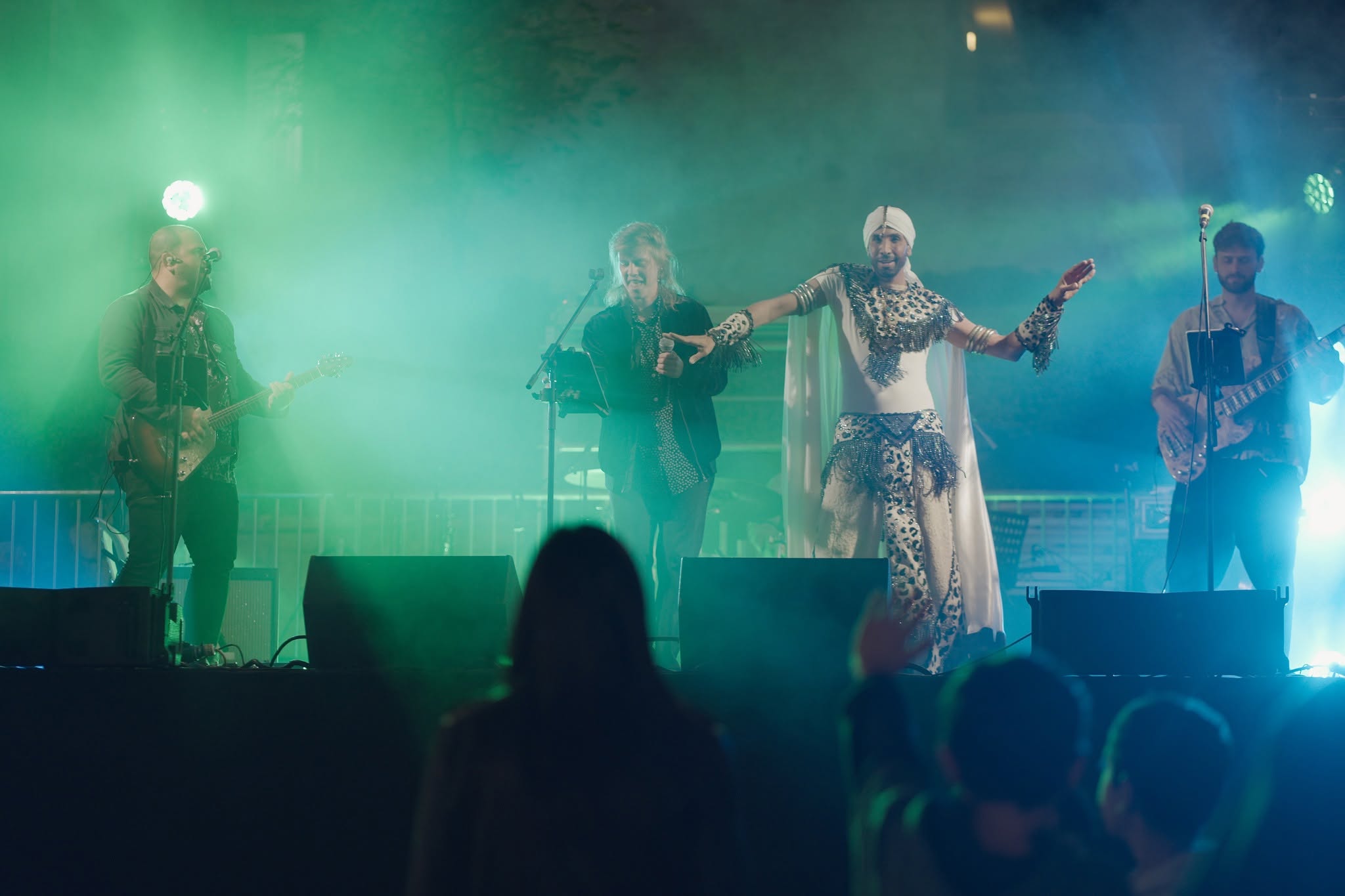 A band performs on a green-lit stage before an audience.