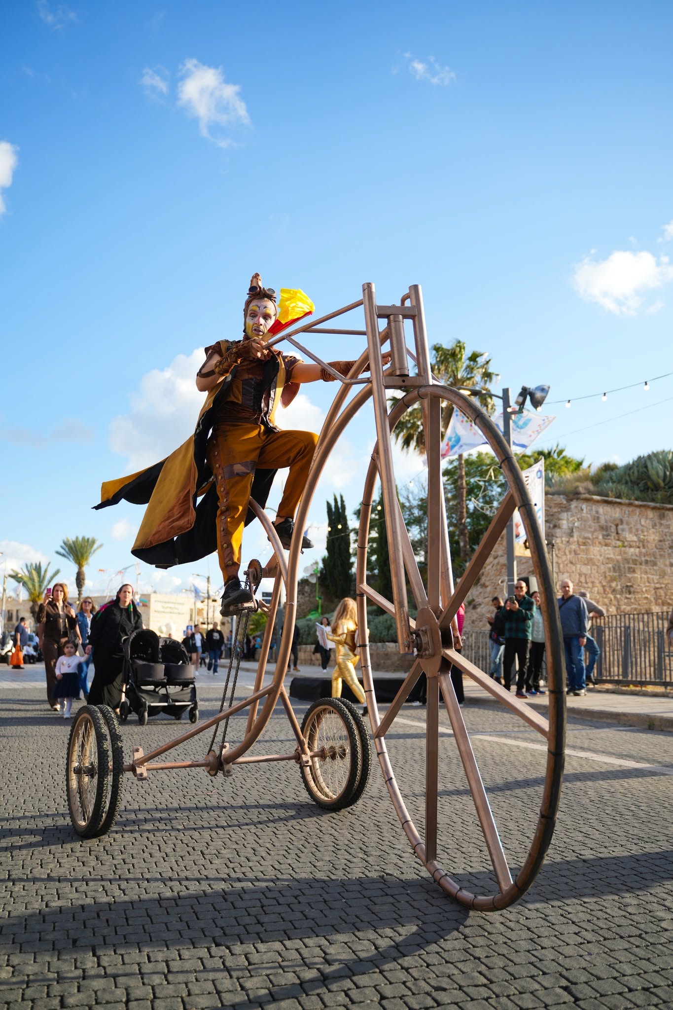 A costumed street performer rides a tall bicycle among visitors.
