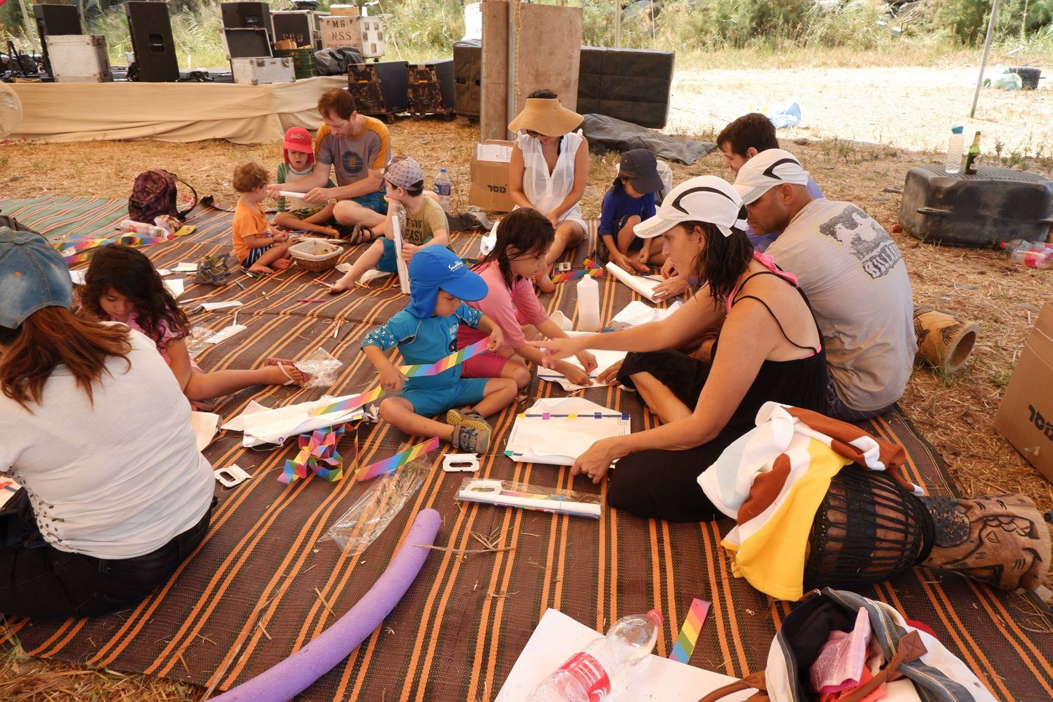 Children and adults take part in a craft workshop on an outdoor mat.