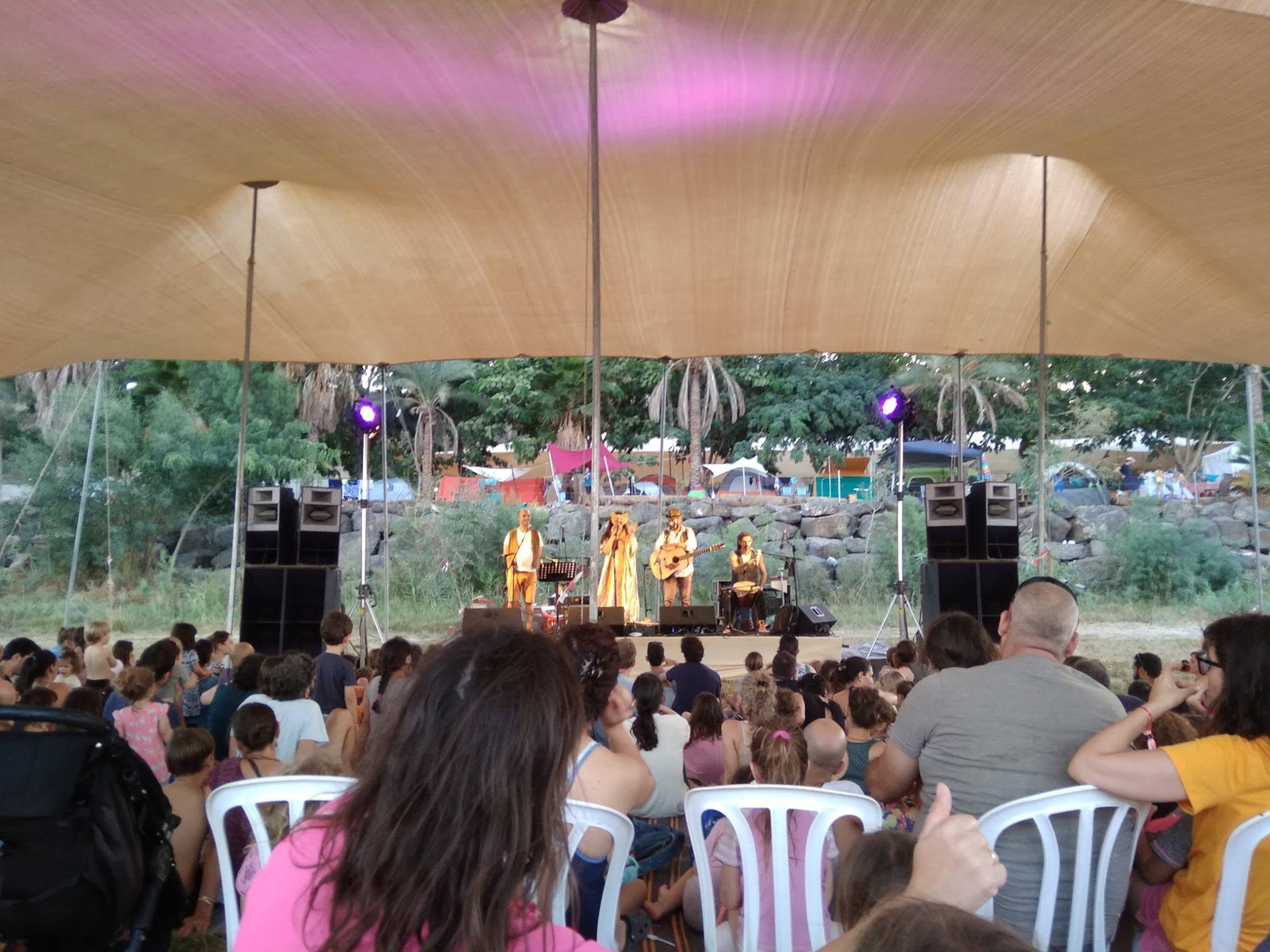 Parents and children watch a stage performance beneath a shade canopy.