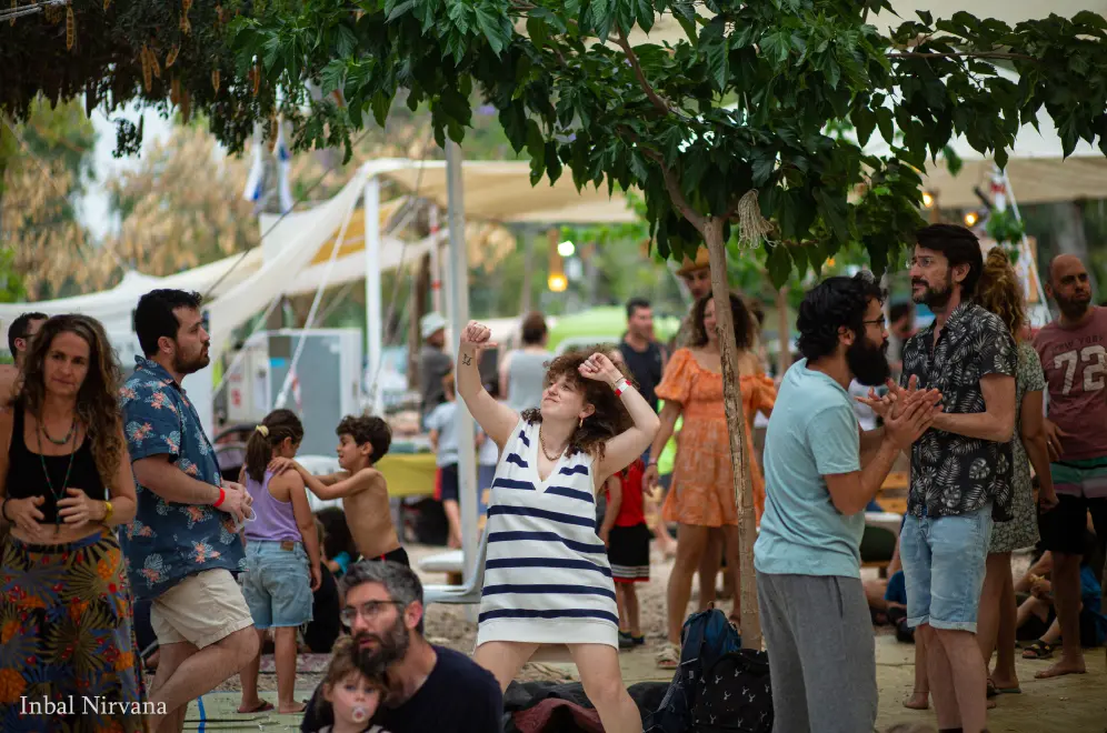 Families dance and gather among trees on the festival grounds.