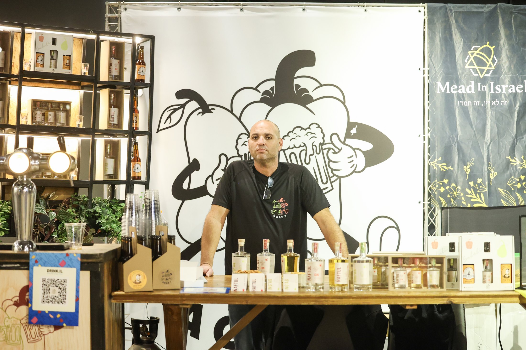An exhibitor stands behind a bottle-lined tasting table.