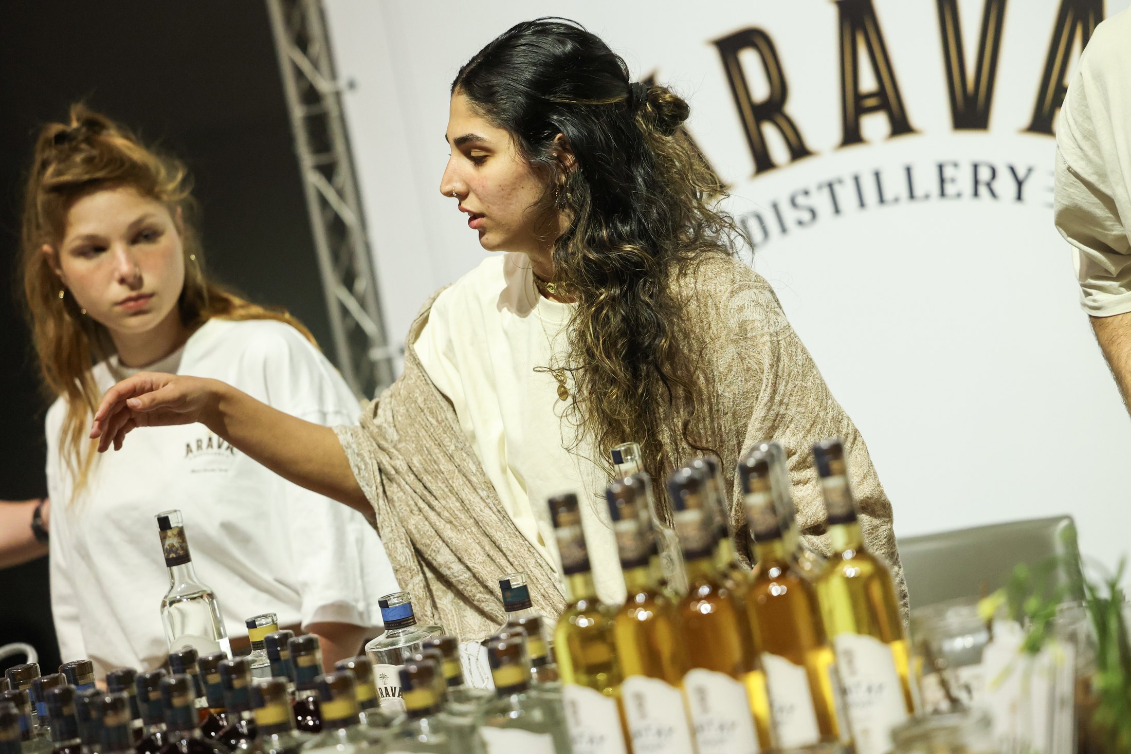 Two exhibitors demonstrate a bottle beside a distillery stand.