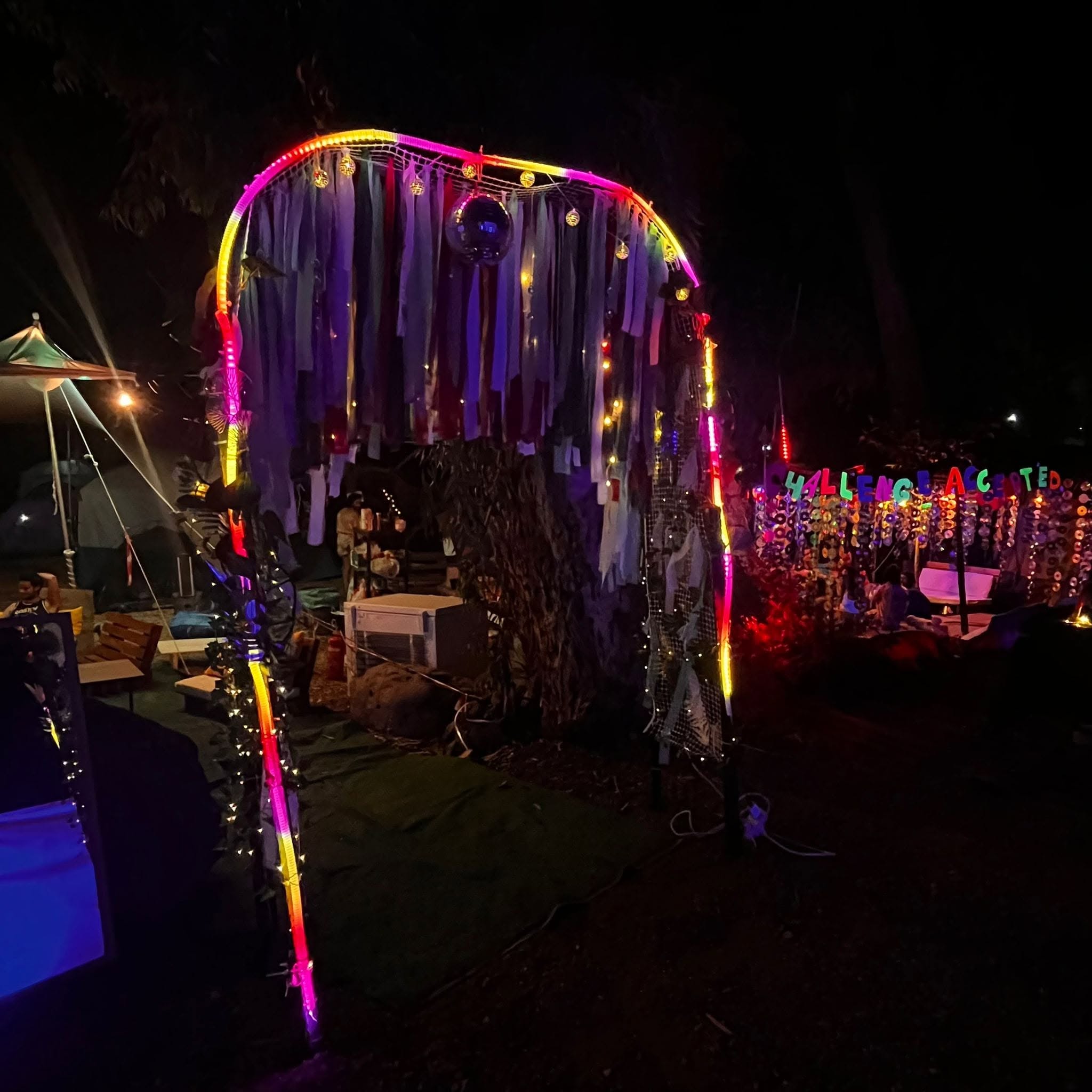 A round structure draped with colourful ribbons glows at night.