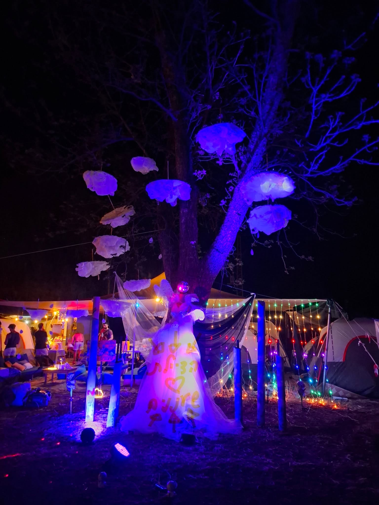 A purple-lit tree with mushroom sculptures hanging from its branches.