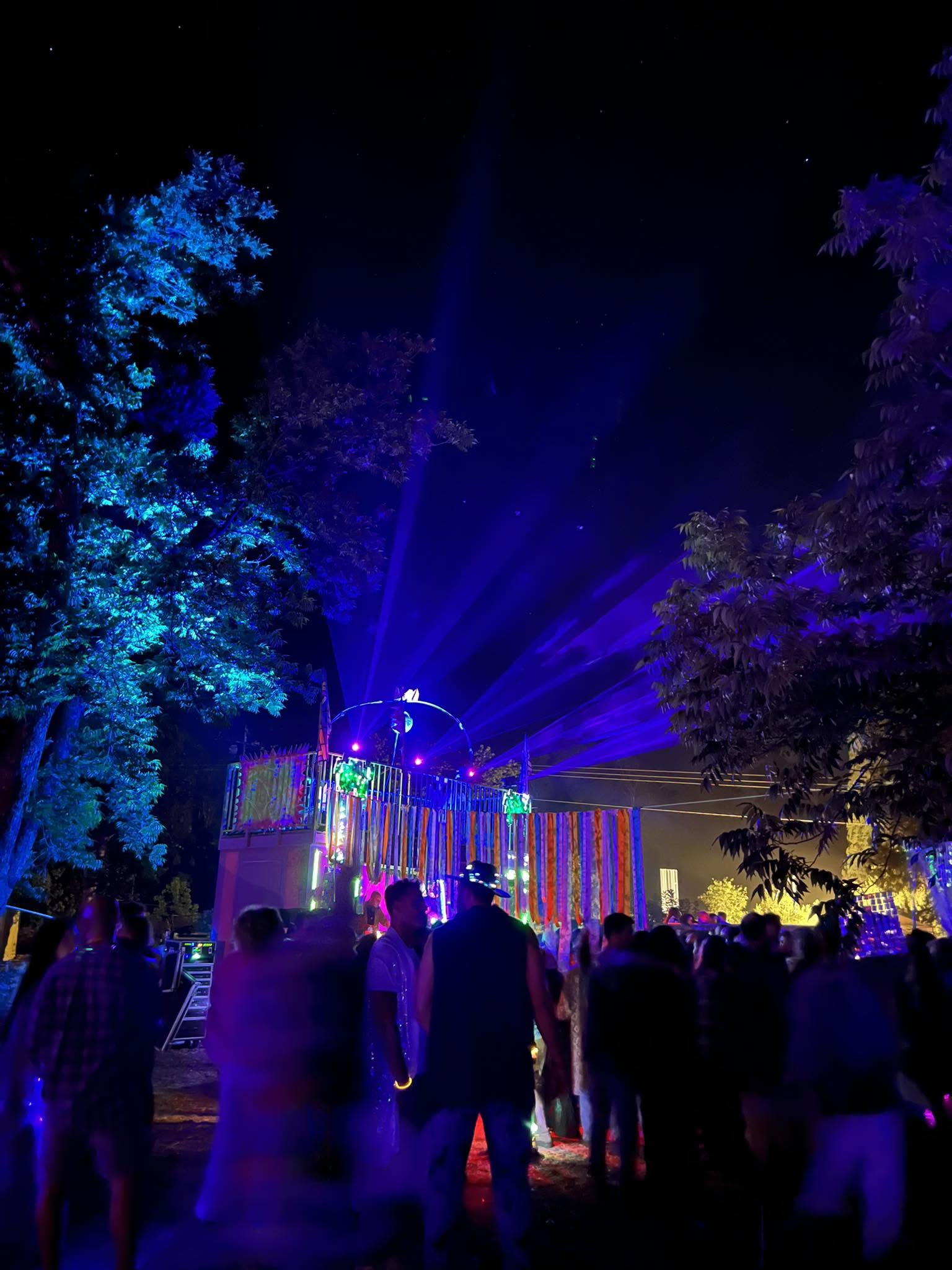 People walk along a path between trees and blue lights.