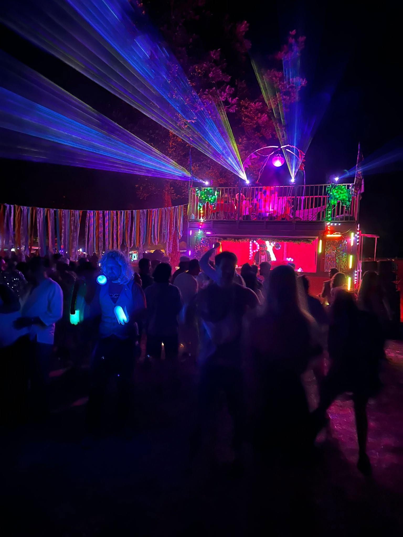 A crowd dances in front of a stage with colourful lasers.