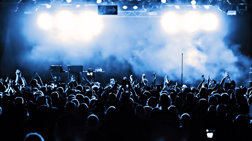 A dense crowd faces a stage lit blue and white.
