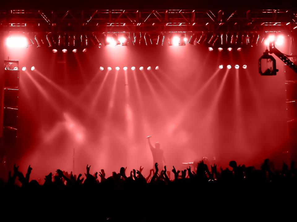 A crowd raises its hands toward a red-lit stage at night.