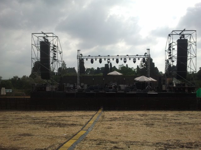 A stage, lighting towers and cables in a field during festival setup.