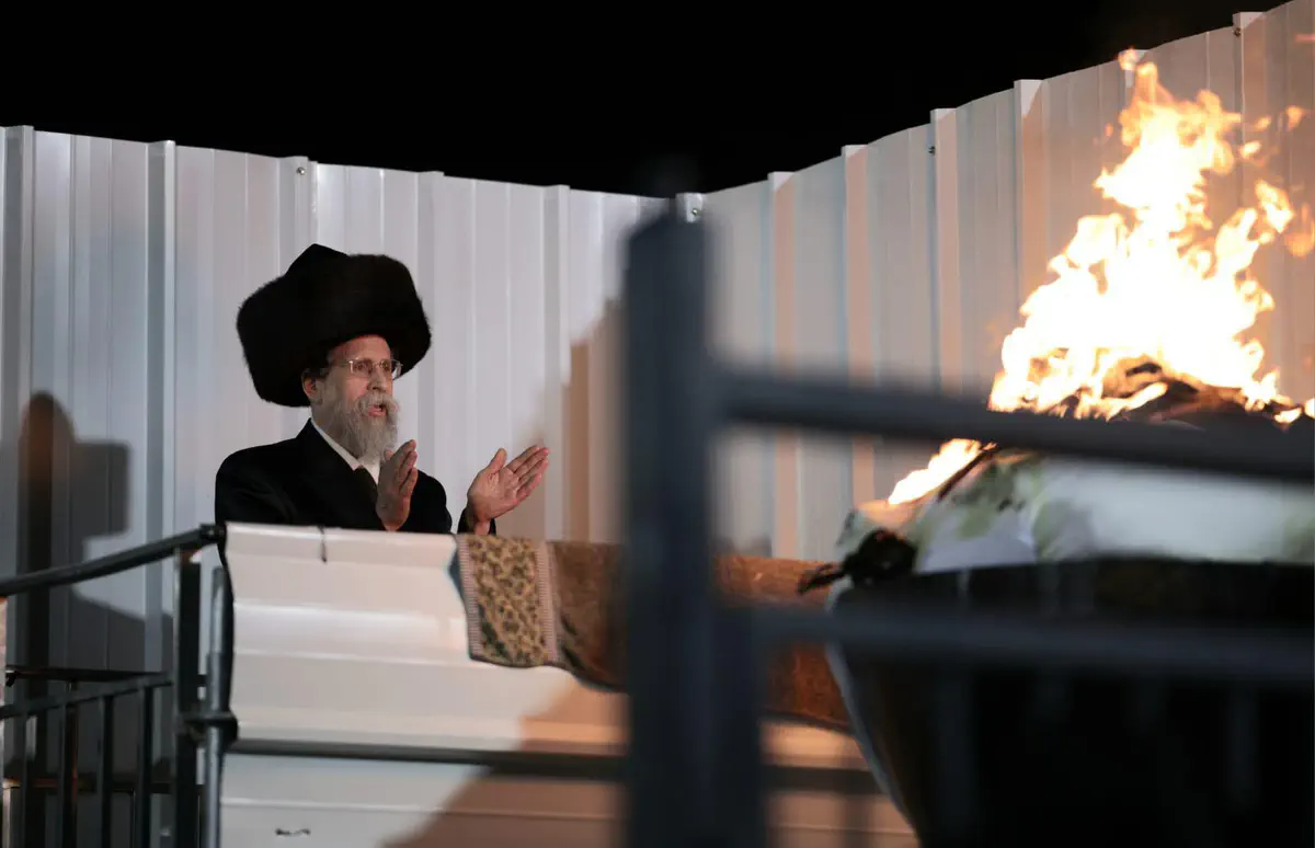 A Hasidic rabbi stands beside the fire during the lighting ceremony.