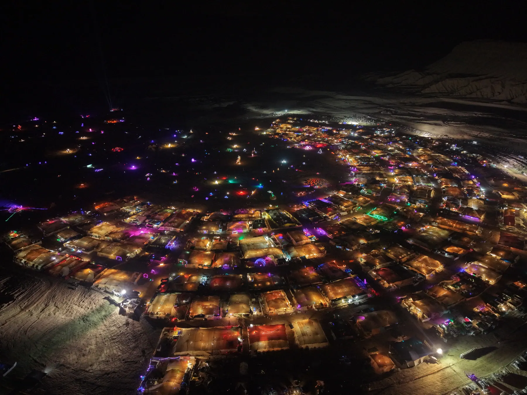 Night-time aerial view of illuminated camps and installations in the desert.