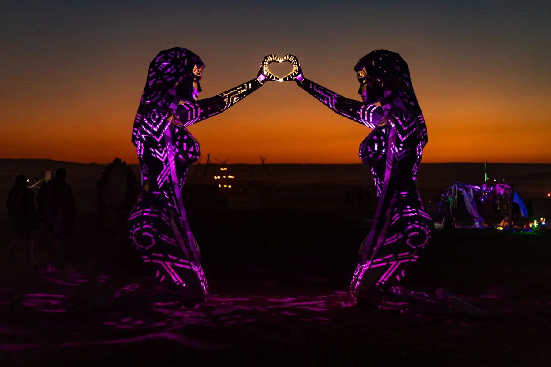 Two purple-lit figure sculptures raise a glowing heart together.