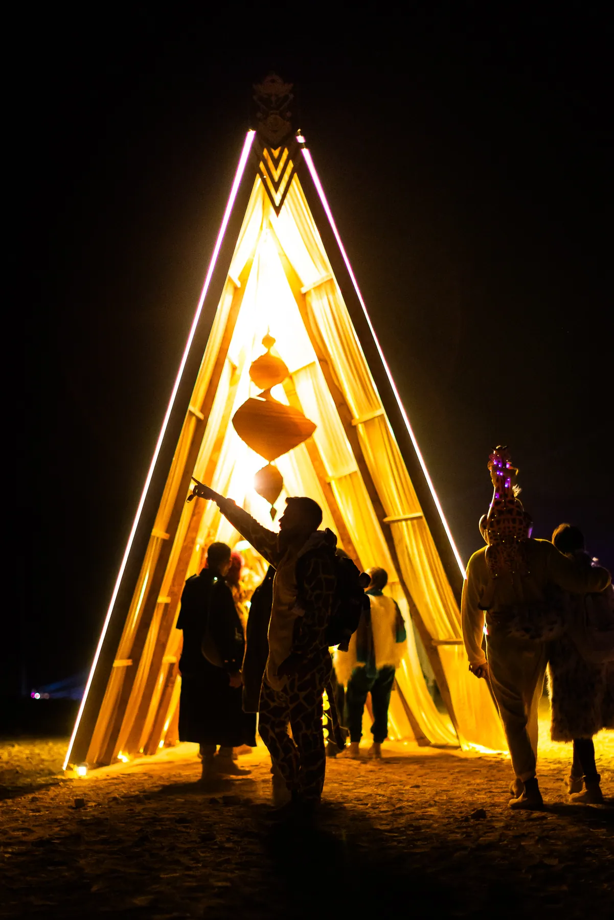Visitors inside a triangular gateway glowing gold at night.