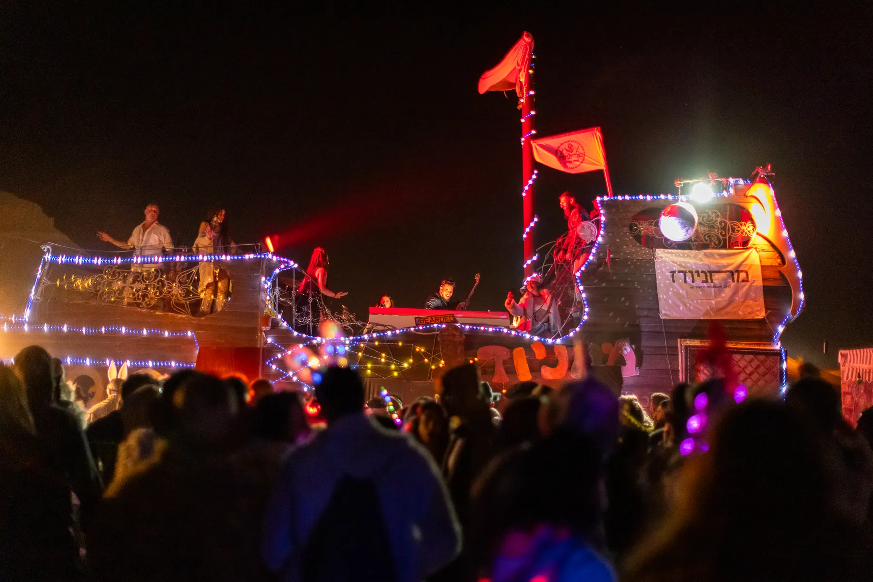 A crowd watches a performance on a lit art vehicle.