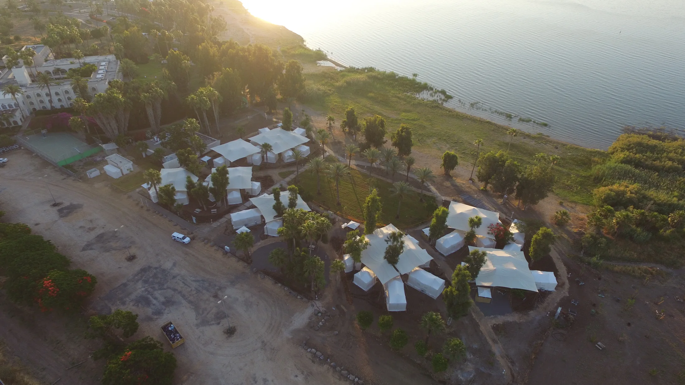 Another aerial view of tents, trees and the shoreline in the evening.