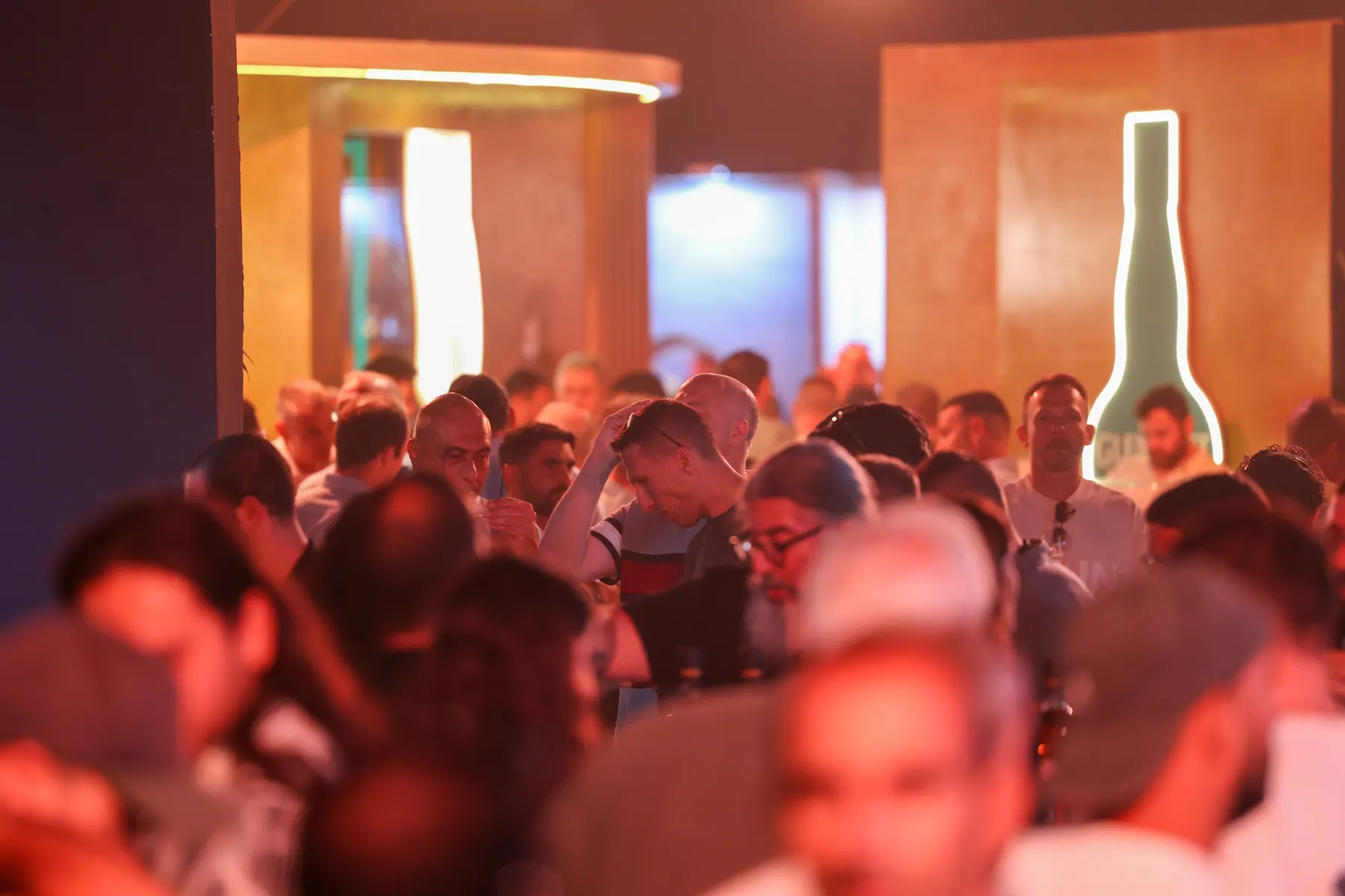 Guests talk in the hall with an illuminated bottle shape behind them.